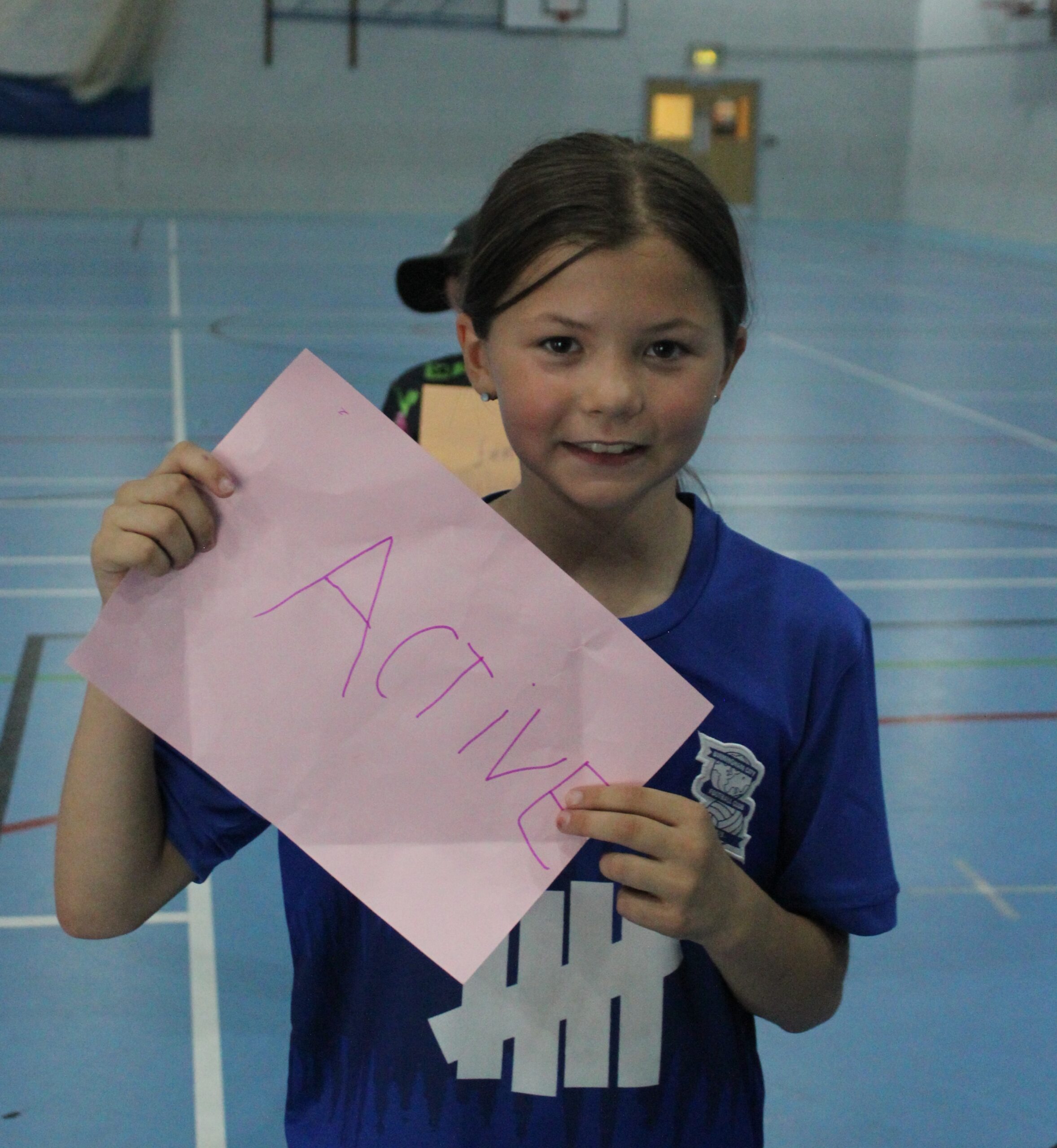 A little girl, dark hair, holding a peace of paper, with the word 'Active' written on it.