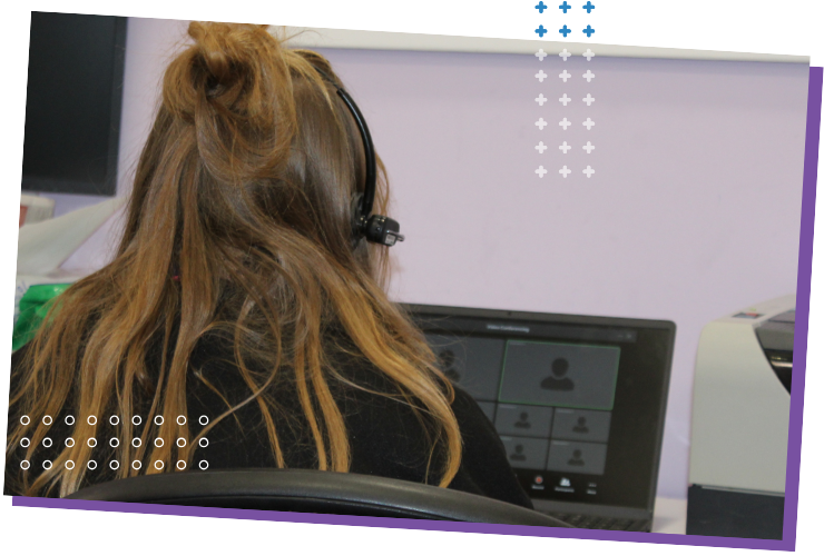 A youth worker with long hair on an online meeting, wearing a headset at a laptop.