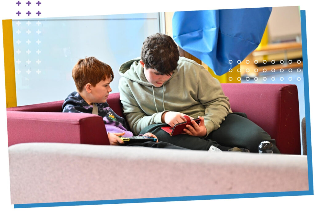 Young people sitting on a sofa using their phone and games console