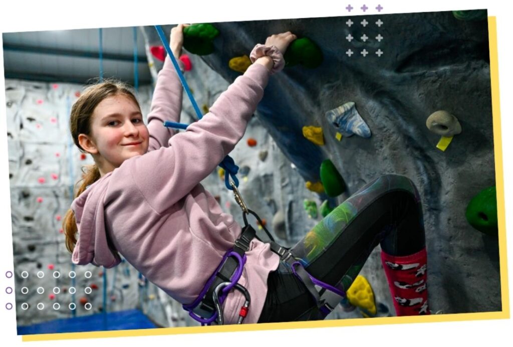 A young girl ascends a rock wall, showcasing her climbing skills and concentration as she navigates the holds.